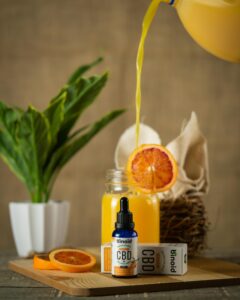 Colorful CBD oil and fresh orange juice on a wooden table, showcasing product photography.